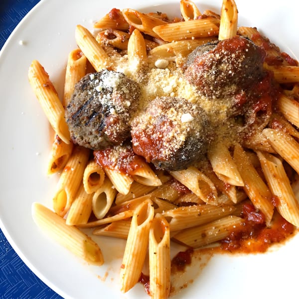 Penne pasta with meatballs, tomato sauce, and grated cheese on a white plate at Goodi's Restaurant.