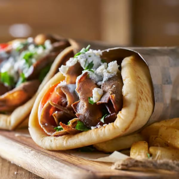 Two Greek gyros with meat, tomatoes, feta cheese, and sauce, served with fries.