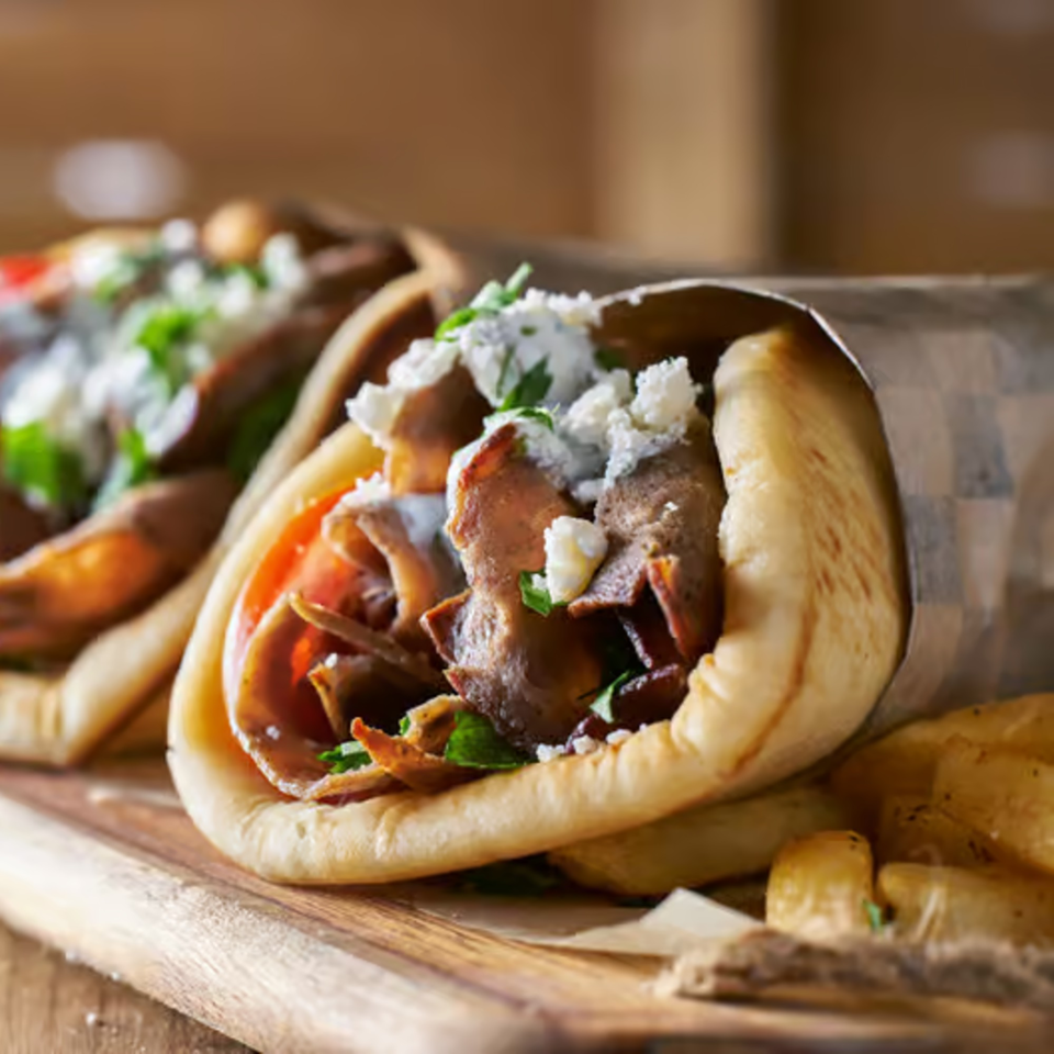 Two Greek gyros with meat, tomatoes, feta cheese, and sauce, served with fries.